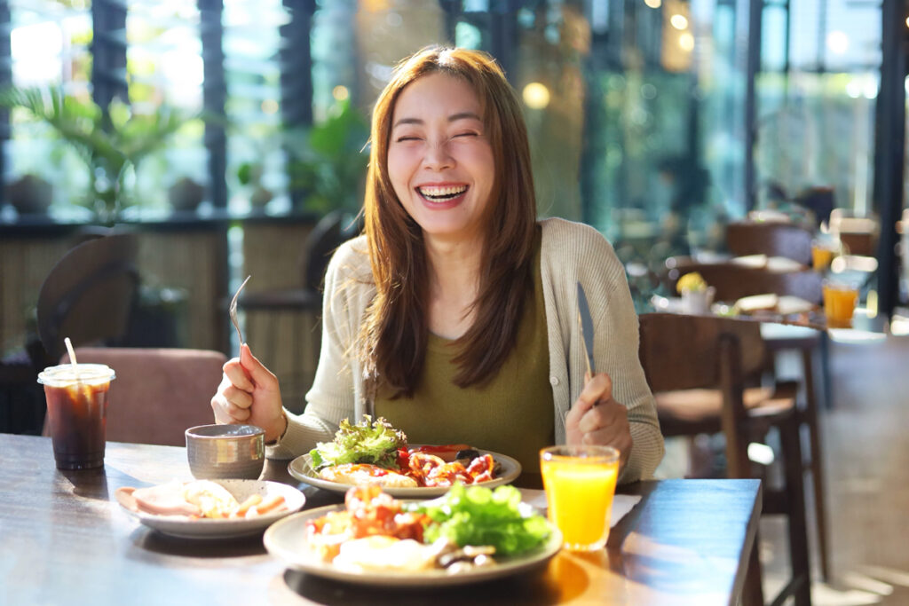 カフェでオレンジジュースとサラダ付きのランチを食べる女性