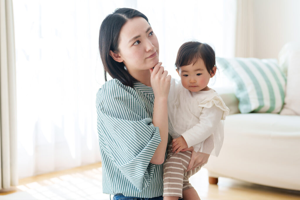 口元に手をやり悩むポーズの女性と抱かれた1歳くらいの子供